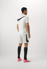 Nike sportfelszerelés, amely egy fehér, rövid ujjú pólóból áll, fekete logóval, hozzá passzoló fehér sorttal, fekete térdzoknikkal és rózsaszín stoplis cipővel.