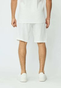 Shorts en lin blanc avec une coupe décontractée, présentant une texture légère et des manches roulées, associés à des baskets blanches et un haut blanc assorti.