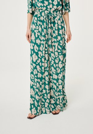 Turkooise wijde broek met witte abstracte bloemenprint, elastische taille met koord, gedragen met bijpassende top en zwarte sandalen met open teen.