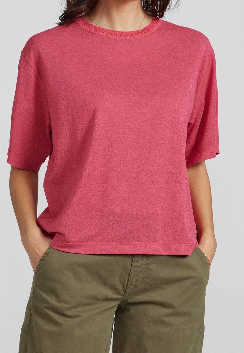 Krátký rukáv, tričko s kulatým výstřihom v bohaté růžové látce, s uvolněným střihem a měkkou strukturou, kombinované s olivově zelenými kalhotami.