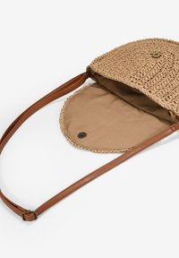 Bolso de paja redondo con un interior de tela beige. Cuenta con una correa de cuero marrón y un cierre de botón. Exterior tejido texturizado.