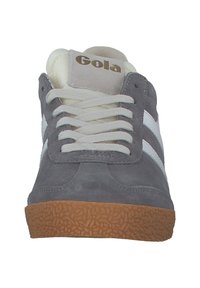 Graue Wildleder-Sneaker mit weißen Streifen, runder Spitze und strukturiertem Gummisohle. Gola-Logo auf der Zunge. Mit flachen weißen Schnürsenkeln geschnürt.