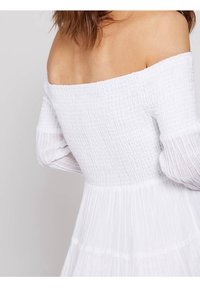 Robe blanche décolletée, avec un corsage texturé, jupe plissée et manches longues transparentes, présentant une taille cintrée et un bas fluide.