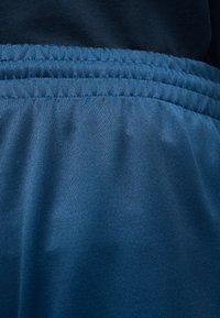 Joustava kuminauha sinisissä kangashousuissa, joissa on kerättyä ompelua, käytetty tummansinisen topin päällä.