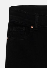 Jeans de ganga pretos com um corte padrão, um pequeno bolso frontal, detalhes em metais cobre e costuras em contraste.