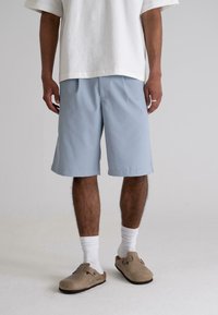 Light blue shorts made of soft fabric, featuring a relaxed fit and side pockets, paired with white socks and beige clogs.