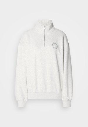 Lys grå genser med halv-zip krage, oversized passform, ribbestrikkede mansjetter og brodert sirkulært tekstaksekt på brystet.