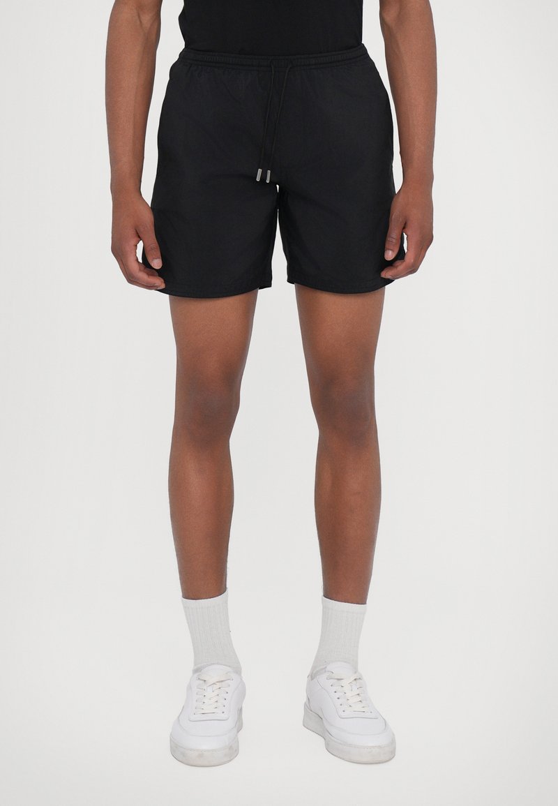 Schwarze Badeshorts mit elastischem Bund und Kordelzug. Hergestellt aus leichtem Material, mit glatter Textur und minimalistischem Design.