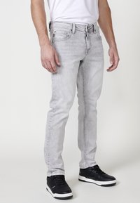 Gai pelēki džinsi ar slim fit piegriezumu, pieci kabatas un nedaudz izbalējuši. Saskaņoti ar melniem sporta apaviem ar baltām zoliņām.