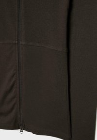 Mörkbrun zip-up jacka av mjukt tyg med stygnsatt paneldesign och en svart dragkedja på vänster sida.