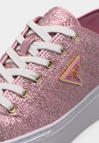 Baskets texturées roses avec lacets blancs, œillets dorés et logo triangulaire Guess USA rose et or sur le côté.