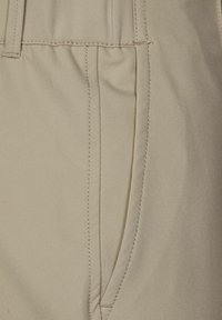Pantaloni in tessuto beige con tasca frontale, cuciture visibili e superficie liscia. Il design è curato con un aspetto pulito e funzionale.