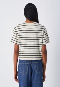Camiseta corta de manga corta en color crema con rayas oscuras; material de algodón; escote redondo; combinada con jeans de mezclilla azul de talle alto con bolsillos traseros.