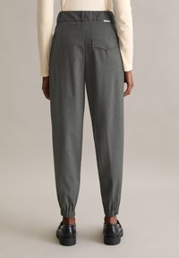 Op maat gemaakte grijze broek met verticale streepjes, elastische tailleband en een enkele achterzak. Afgewerkt met ribbels aan de taille en platte naden.