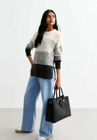 Pull rayé gris et blanc à coupe décontractée, associé à un jean large bleu clair et un sac à main noir. Texture lisse et design moderne.