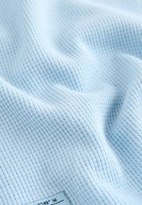 Tela azul claro con textura de gofre y una pequeña etiqueta en la esquina que muestra coordenadas en texto negro.