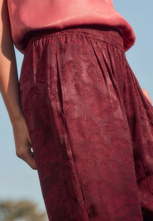 Pantalons plissés bordeaux avec une taille élastique, ornés d'un motif de feuilles texturé sur un tissu lisse et léger.