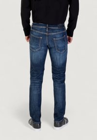 Jeans in denim blu scuro visti da dietro, con due tasche posteriori caratterizzate da un motivo di cucitura sottile e un design a vestibilità dritta.
