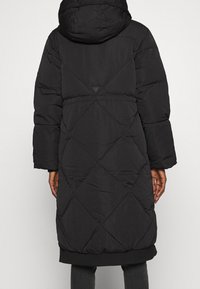 Černá péřová bunda s kapucí, design s diamantovým prošíváním, dlouhé rukávy, elastické manžety a žebrovaný lem. Na zadní straně je detaily s logem.