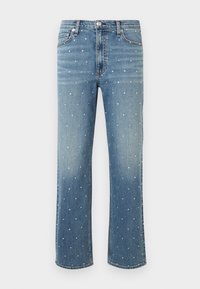 Jean en denim bleu avec jambes droites, décoré de petits clous argentés répartis uniformément sur tout le tissu.
