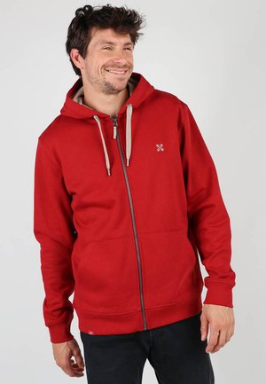 Haut de survêtement zippé rouge avec capuche à cordon, poches avant et accents beiges contrastants. Fabriqué en tissu doux avec une texture lisse.