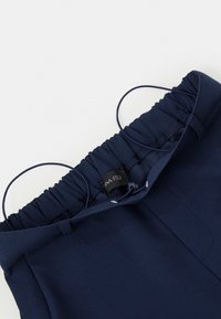 Marineblauwe broek met een elastische tailleband en een zwart merkembleem, met trekkoordlussen op een witte achtergrond.