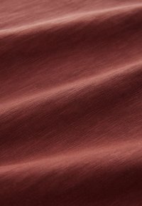 Mostră de țesătură texturată într-o nuanță caldă maro-roșiatică, cu variații subtile de culoare și o suprafață moale și netedă.