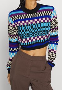 Geschnittenen Strickpullover mit lebhaften geometrischen Mustern in Blau, Lila und Schwarz. Mit einem schwarzen gerippten Kragen und bunten gestreiften Bündchen.