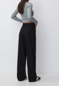 Striped long-sleeve top with a fitted cut, paired with high-waisted, wide-leg black trousers featuring a back pocket and button detail.