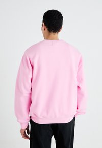 Růžová mikina s uvolněným střihem, žebrovanými manžetami a lemem, vyrobená z měkké látky. Zadní část má jednoduchý design bez grafiky.