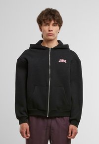 Felpa nera con zip realizzata in misto cotone. Presenta una tasca frontale, polsini aderenti e un logo rosa sul petto. Senza motivi né dettagli decorativi.