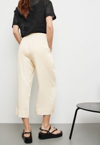 Pantalons courts crèmes à jambe large, avec ourlet cousu et taille élastique, associés à des sandales à plateforme noires et un haut perforé noir.