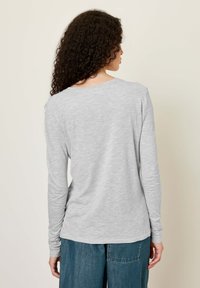 Pelēks garām piedurknēm krekls ar apaļu kakla izgriezumu un brīvu piegriezumu. Mīksts, teksturēts audums ar smalkām krāsas variācijām, kopā ar vaļīgām zilām džinsa biksēm.