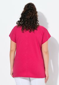 Haut fuchsia à manches courtes avec une coupe décontractée, présentant une texture douce et un ourlet arrondi, affiché de dos sur un fond uni.