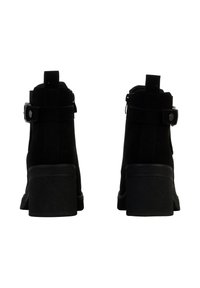 Bottines en suède noir avec un talon épais, fermeture éclair, et une sangle décorative avec un détail en clou métallique.