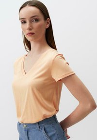 T-shirt pesca a scollo a V realizzata in tessuto morbido, con maniche corte e vestibilità comoda, abbinata a jeans azzurri a vita alta.