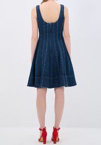 Denimmekko, jossa on muodikas yläosa ja levenevä hame, näyttävällä pyöreällä selällä ja näkyvillä saumoilla. Yhdistetty punaisiin korkokenkiin.