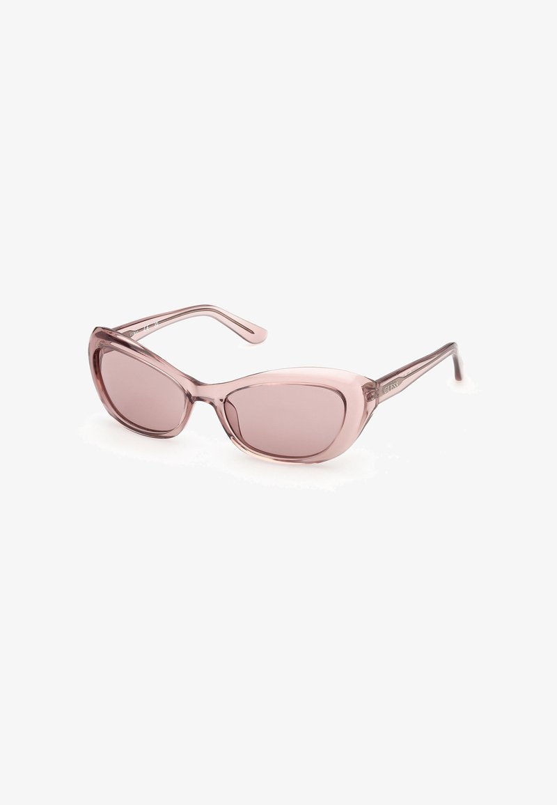 Lunettes de soleil cat-eye translucides roses avec verres teintés, inclinées pour montrer la branche gauche embossée du nom de la marque.