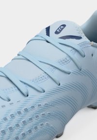 Svetlo modri športni čevelj s vezalkami, teksturirano površino in logotipom "F72" na jezičku, namenjen za zunanjo uporabo.