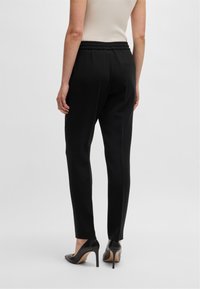 Pantaloni neri con una vestibilità ampia, vita elastica e gambe affusolate, abbinati a scarpe con tacco nere. Vista posteriore presentata.