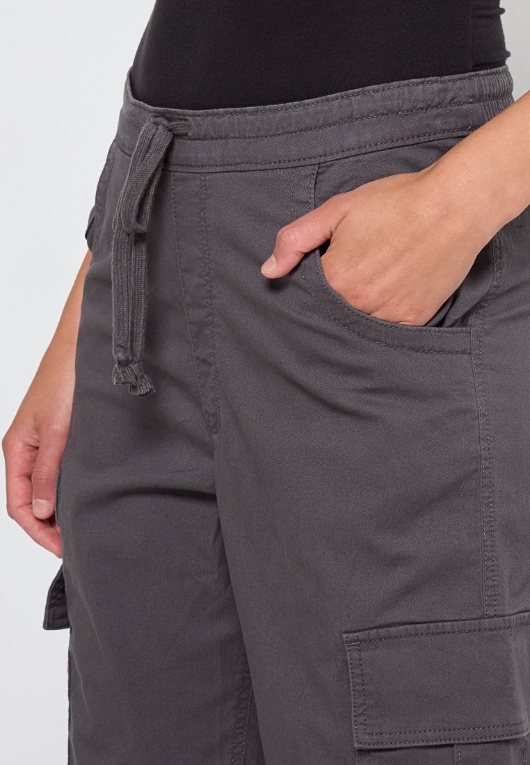 Szare bawełniane spodnie cargo z elastycznym pasem, szczegółami sznurowania, boczną kieszenią oraz dużą kieszenią cargo na nodze.