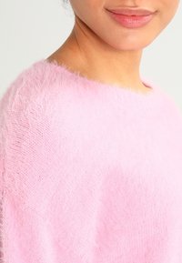 Pull doux et moelleux rose pâle avec un large décolleté et une coupe ample, présentant un motif tricoté délicat et texturé.