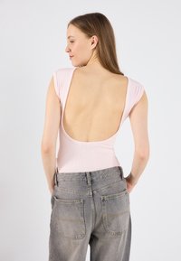 Roza rebrasta bodysuit z globokim izrezom na hrbtu in kratkimi rokavi, v kombinaciji z visokim pasom sivih kavbojk z zadnjimi žepi in detajli šivanja.