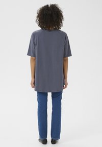 T-shirt grigia con maniche raglan corte, vestibilità rilassata e orlo arrotondato, abbinata a jeans blu a gamba dritta e calzature nere.