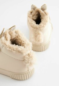 Beige faux leather ankle boots with fluffy beige trim, rounded shapes, small ears on the top, and textured rubber soles.