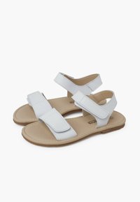 Sandales blanches avec une semelle plate, deux sangles Velcro réglables et une texture lisse. La semelle intérieure est de couleur beige clair.