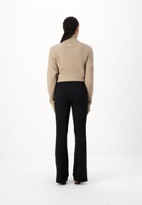 Un pull à col roulé côtelé beige associé à un pantalon noir évasé. Le pull présente un design court et des épaules tombantes.