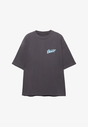 Tricou supradimensionat gri, din bumbac, cu un logo grafic albastru pe partea stângă a pieptului, guler rotund și mâneci scurte.