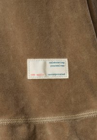Smeđi materijal s mekom teksturom sadrži ušivenu oznaku. Oznaka uključuje tekst "odd molly", "slavimo sebe" i "neincorporirana".