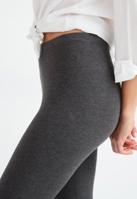 Grijze leggings van zacht, rekbaar materiaal, met een hoge tailleband en een gladde textuur, zijwaarts getoond met een wit shirt.